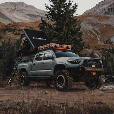 freespirit-recreation-aspen-v2-standard-hard-shell-roof-top-tent-black-open-front-corner-view-on-toyota-tacoma-with-woman-in-nature