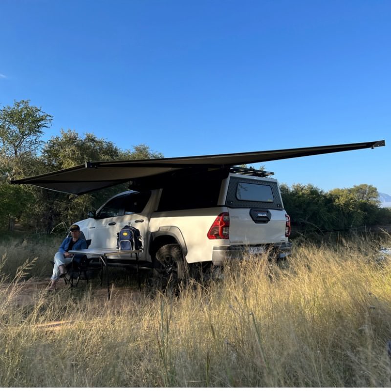 eezi-awn-dragonfly-180-open-gray-free-standing-rear-corner-view-on-toyota-tundra-with-person-in-nature