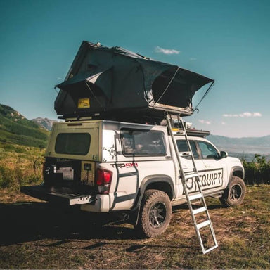 eezi-awn-sabre-hard-shell-roof-top-tent-open-rear-corner-view-on-vehicle-with-extended-rods-and-ladder-in-field