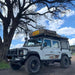 eezi-awn-series-3-roof-top-tent-beige-closed-front-corner-view-on-land-rover-defender-under-tree