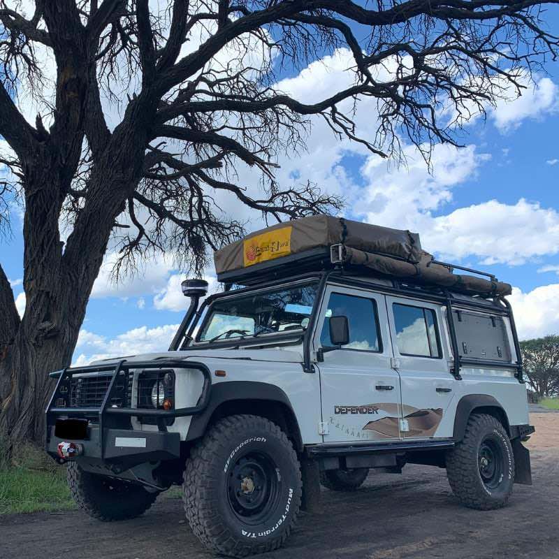 eezi-awn-series-3-roof-top-tent-beige-closed-front-corner-view-on-land-rover-defender-under-tree