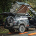 eezi-awn-series-3-soft-shell-roof-top-tent-olive-open-rear-corner-view-on-vehicle-with-person-in-nature-closing-tent