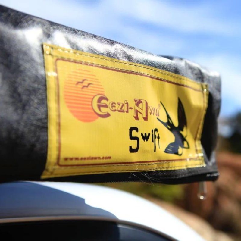 eezi-awn-swift-awning-beige-close-front-corner-view-close-up-on-vehicle-with-brand-logo-in-nature