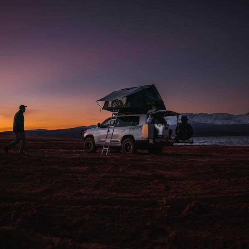 eezi-awn-sword-hard-shell-roof-top-tent-open-rear-corner-view-on-vehicle-with-person-in-sandy-beach