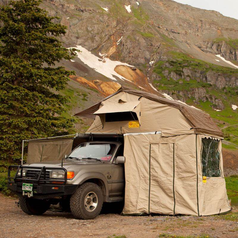 eezi-awn-xklusiv-soft-shell-roof-top-tent-beige-open-front-corner-view-on-vehicle-with-extended-room-and-big-windows-in-the-mountains