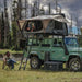 overland-vehicle-systems-bushveld-hard-shell-roof-top-tent-open-front-corner-view-on-land-rover-defender-at-lake-side-with-persons-camping