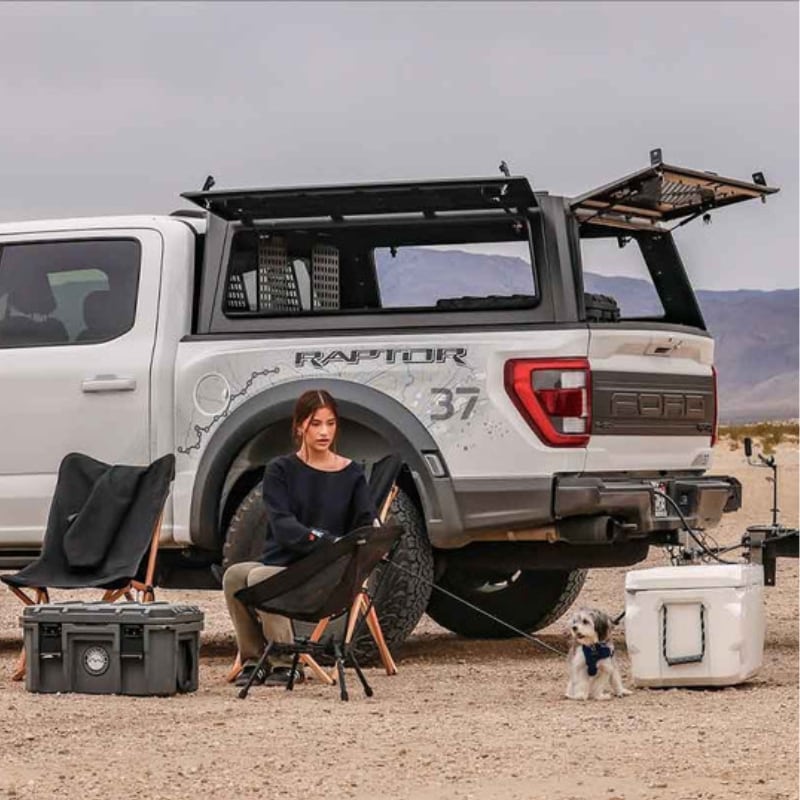 overland-vehicle-systems-expedition-truck-cap-for-ford-f-150-black-open-rear-corner-view-on-ford-raprtor-with-person-camping