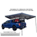 overland-vehicle-systems-nomadic-lt-270-awning-with-walls-dark-gray-open-driver-side-rear-view-on-ford-ranger-stx-two-fixed-pivoting-and-telescoping-aluminum-poles