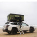 tentbox-classic-2-hard-shell-roof-top-tent-forest-green-open-front-view-on-subaru-outback-with-person-on-ladder-at-the-beach