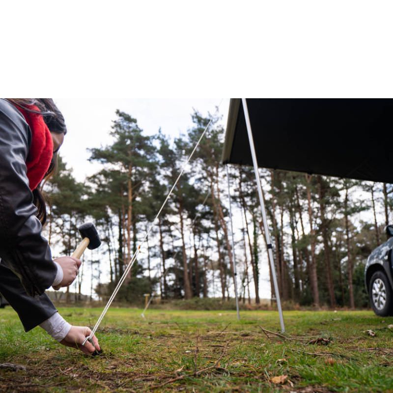 tentbox-universal-side-awning-open-close-up-view-with-person-hammering-the-peg-into-the-ground-in-nature