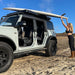 badass-tents-recon-pop-up-roof-top-tent-closed-side-view-person-loading-surfboard-on-crossbars-on-ford-bronco